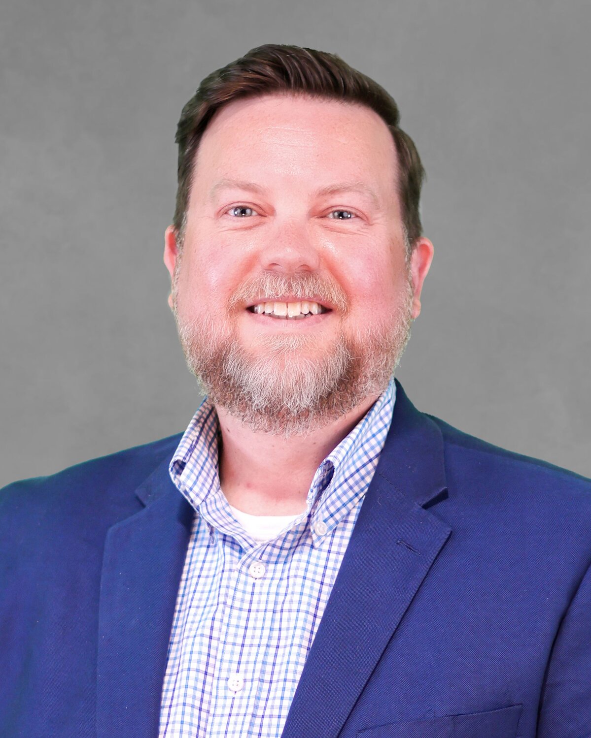 Person wearing a blue blazer over a checkered button-up shirt, posed against a plain gray background